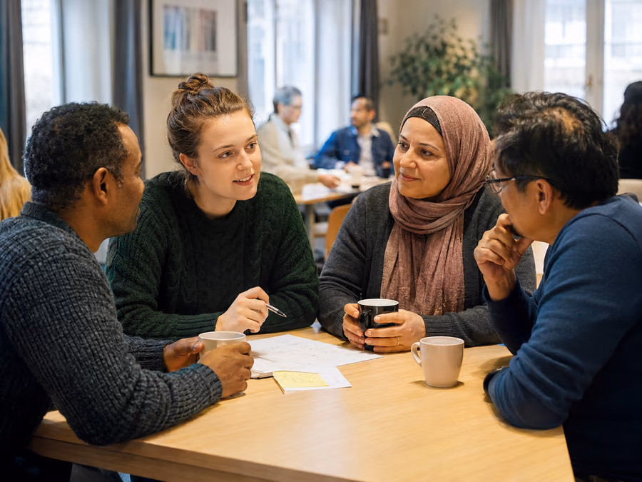 Student og deltakere i samtale rundt et bord på språkkafé